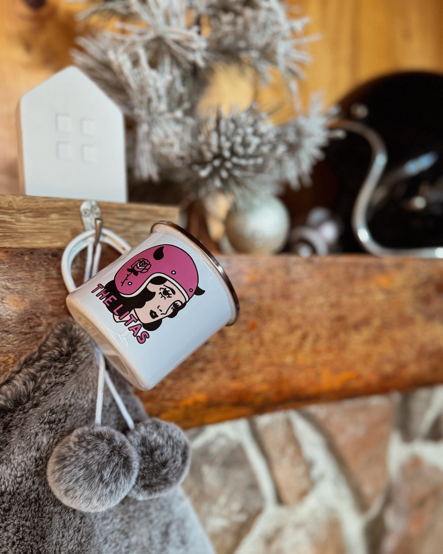 White enamel Litas  mug with a pink She Davile design hanging on a mantle with Christmas decorations